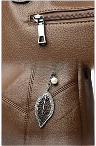 Close-up of leather handbag with silver zipper and leaf-shaped metal pendant with pearl