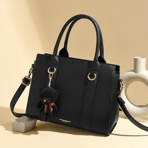 Sac à main élégant en cuir noir grainé avec détails dorés et pendentif ours