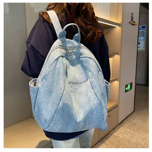 Detailed back view of a light blue denim backpack with punk rivet accents on a model