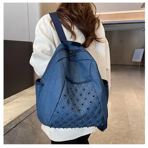 Detail of dark blue denim backpack with punk style metal rivets and side pocket shown on model