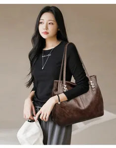 Detail of vintage brown leather tote bag showing textured surface and metal M buckle