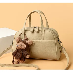 Close-up of beige lychee grain leather Boston bag with metal zippers and cute bear charm