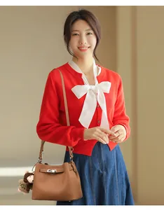 Detail of red knitted cardigan featuring a large white bow tie and ribbed cuffs