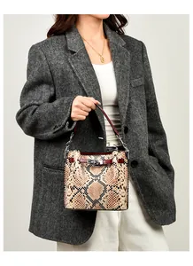 Detalle de bolso bucket de piel de serpiente con cierre plateado sobre traje gris