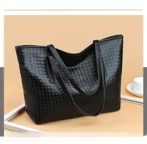 Detail of black woven leather tote bag with shoulder strap and coffee cup prop