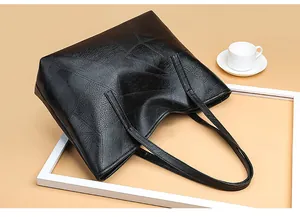 Detailed top view of a black woven leather tote bag with long straps on a beige background
