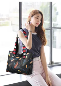 Detail of large black tote bag with feather print and colorful striped strap on shoulder
