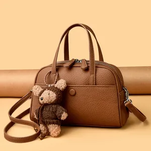 Brown litchi grain Boston bag with top handles, crossbody strap and a small bear charm