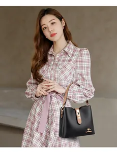 Detail of black leather bucket bag with gold clasp and brand logo on checkered dress