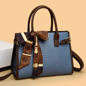 Bolso de cuero azul con relieve de serpiente, asas marrones y un pañuelo de seda adornado