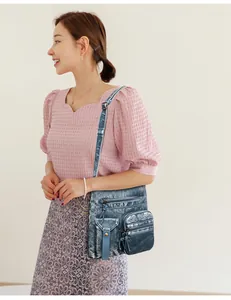 Close-up of vintage blue denim leather bucket bag with multiple zippers on a female model