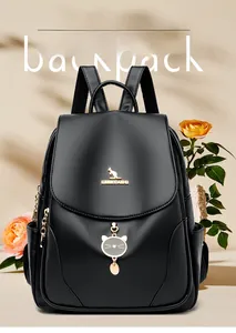 Dettaglio zaino in pelle nera con logo a canguro dorato e ciondolo a forma di gatto su beige