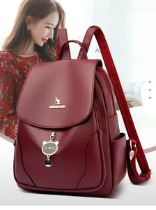 Dettaglio dello zaino in pelle bordeaux con logo a canguro dorato e ciondolo a forma di gatto