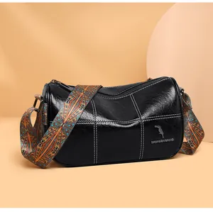 Close-up of black cylinder bag with white stitching and colorful woven shoulder strap