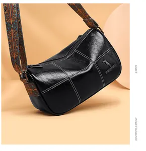 Detail of black leather barrel bag featuring white stitching and colorful ethnic strap