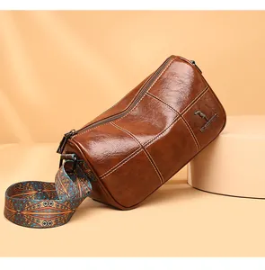 Detail of retro brown leather cylinder bag with contrast stitching and patterned strap