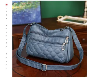Detail van blauwe crossbodytas met drievoudige ritssluiting en ruitvormig stiksel
