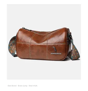 Detail of dark brown leather cylinder bag featuring contrast stitching and bird metal logo