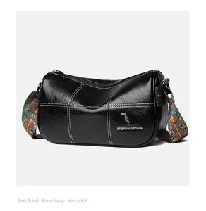 Detail of black leather barrel bag featuring white stitching and ethnic patterned strap