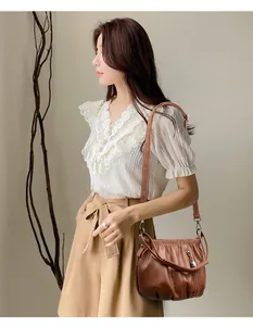 Brown soft leather bucket bag with pleats and metal charm styled on a model in white lace top