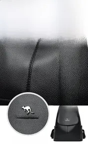 Close-up of black litchi grain leather texture and metallic kangaroo logo on the backpack