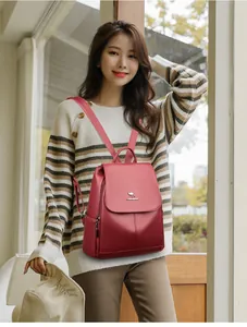 Close-up of red leather backpack featuring metal kangaroo logo on a striped sweater