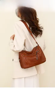 Detail of soft brown leather crossbody bag with multiple zippers shown on a model