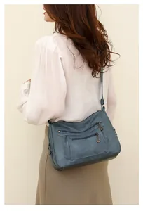 Blue soft leather crossbody bag side view on model with double zipper detail pockets