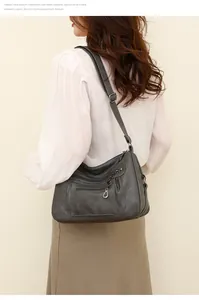 Detail of gray soft leather crossbody bag with multiple zippers worn by a model