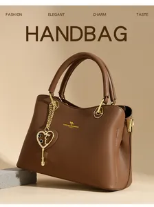 Nahaufnahme der Ledertextur mit goldenem Känguru-Logo und Herzanhänger an brauner Handtasche