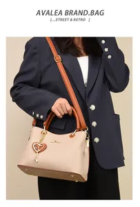 Detail der beigen Lederhandtasche mit braunen Griffen und herzförmigem Anhänger