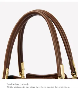 Detailed macro view of the brown lychee leather handle with polished gold metal buckles