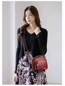 Detail of burgundy leather crossbody bag with multi-zipper layers and gold heart charm