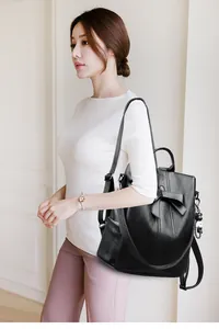 Detail eines schwarzen Lederrucksacks mit dekorativer Schleife und süßem Puppenanhänger