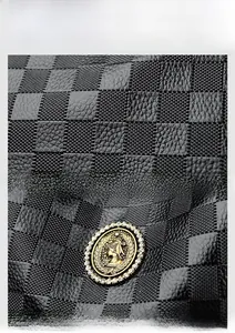 Détail du cuir gaufré à damier noir avec un emblème doré orné de strass brillants