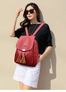 Detailed view of the dark red leather backpack featuring metal logo and floral tassel accents