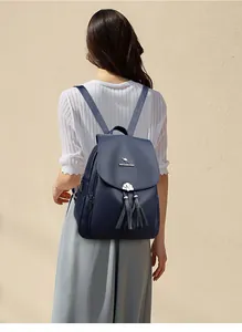 Detail view of navy blue faux leather backpack featuring silver shell charm and long tassels