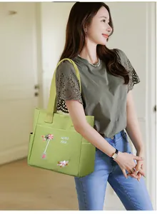 Dettaglio del ricamo floreale e tasca laterale su una borsa tote in tela verde