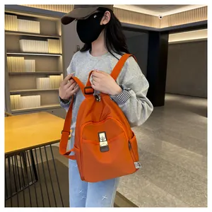 Detail of bright orange nylon backpack with silver lock and buckle on a side-wearing model