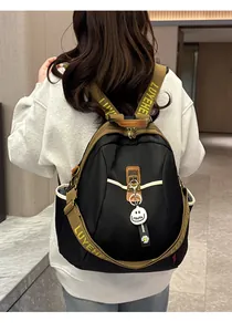 Détail d'un sac à dos noir en nylon avec sangles vertes, poches latérales et pendentifs