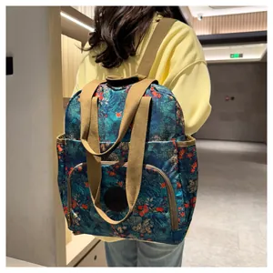 Blue floral backpack with brown nylon straps worn by a model in a modern indoor hallway