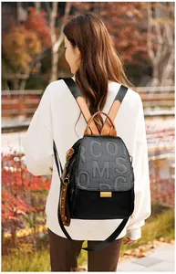 Detail of black pebbled leather backpack with embossed letters and studded brown strap