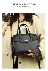 Dettaglio di una borsa in pelle nera con logo a canguro dorato, indossata da una modella in trench