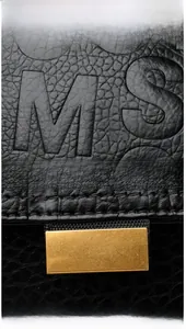 Detail of black lychee grain leather backpack with golden metal buckle and embossed letters