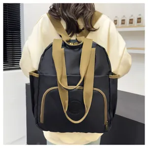 Detail view of the black nylon backpack with khaki webbing straps worn by a model