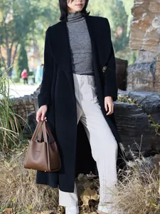 Outdoor shot of a woman in a black wool coat holding a coffee brown leather bucket bag