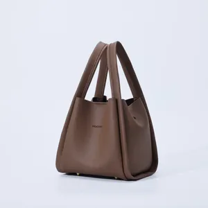 Detail view of dark brown litchi grain leather texture and golden metal feet on bucket bag