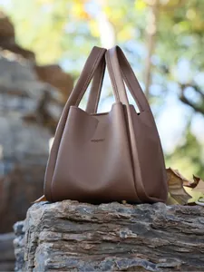 Detail of dark brown lychee grain leather bucket bag with HOCOMU logo on natural rock
