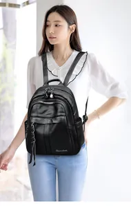 Detail of black litchi pattern leather backpack featuring silver zippers and long tassels
