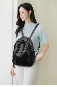 Side view of a black lychee texture leather backpack worn by a model in a casual setting
